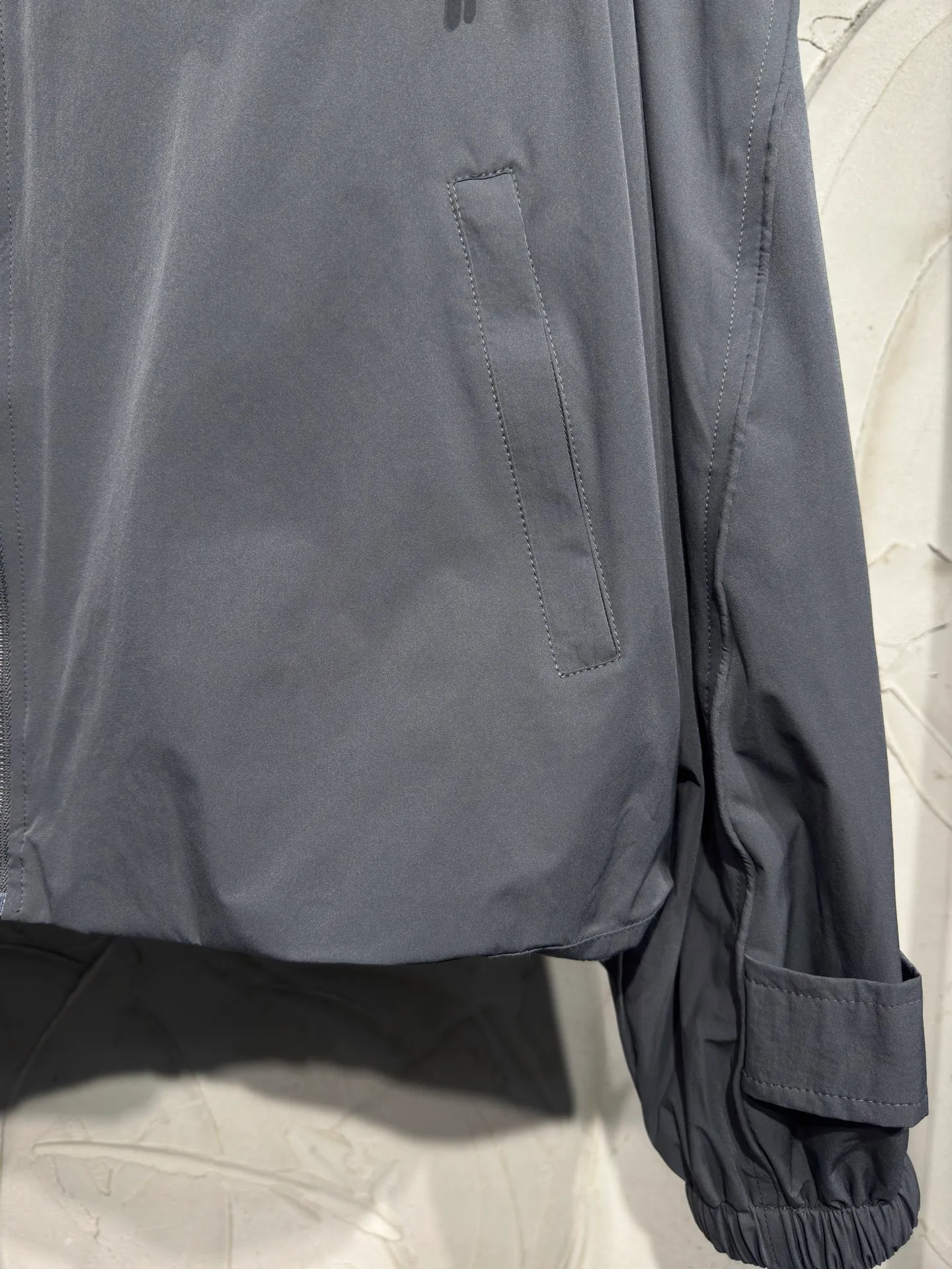 Acne Studios 26SS Large Lapel Short Jacket The fabric is made of 100% nylon (nylon/polyamide fiber) 75D high-density wrinkled nylon. The fabric has been permanently pressed and shaped by high temperature, and washed with high-pressure wrinkles at the factory to form its own irregular texture, permanently retaining the wrinkled texture, which will not disappear after washing. Matte matte coating removes the plastic glossy surface of nylon itself to create a low-key matte paper feel. Three-proof micro-coating, weak waterproof, anti-fouling, anti-static treatment, not easy to get dust. The interior is made of full-width mesh Breathable nylon lining, which reduces the stickiness of the nylon fabric to the body, improves air circulation, prevents sweating from sticking to the skin, and the zipper does not rub against the skin. The version adopts the raglan split topstitching process, and the front and rear panels are divided diagonally to expose even stitching. The three-dimensional dropped shoulders are loose and the fit is increased to increase the margin of movement. The back neckline is three-dimensional and high-density computer embroidered, and the embroidery lines are dense and not prickly. Customized all-metal matte nylon zipper, Genuine Leather embossed brand letters on the zipper leather tab, zipper tape with same color nylon fit to the body, double-locked reinforcement on both sides of the zipper to prevent pulling and tearing. Color: Gray Size: S M L